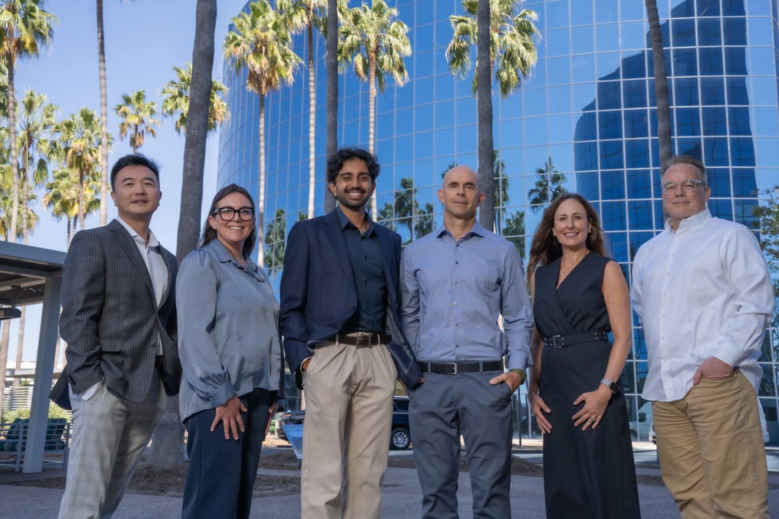 OG Advisors Team – Outdoor Group Portrait (Close) The six-person OG Advisors team outdoors in front of a glass office tower and palm trees